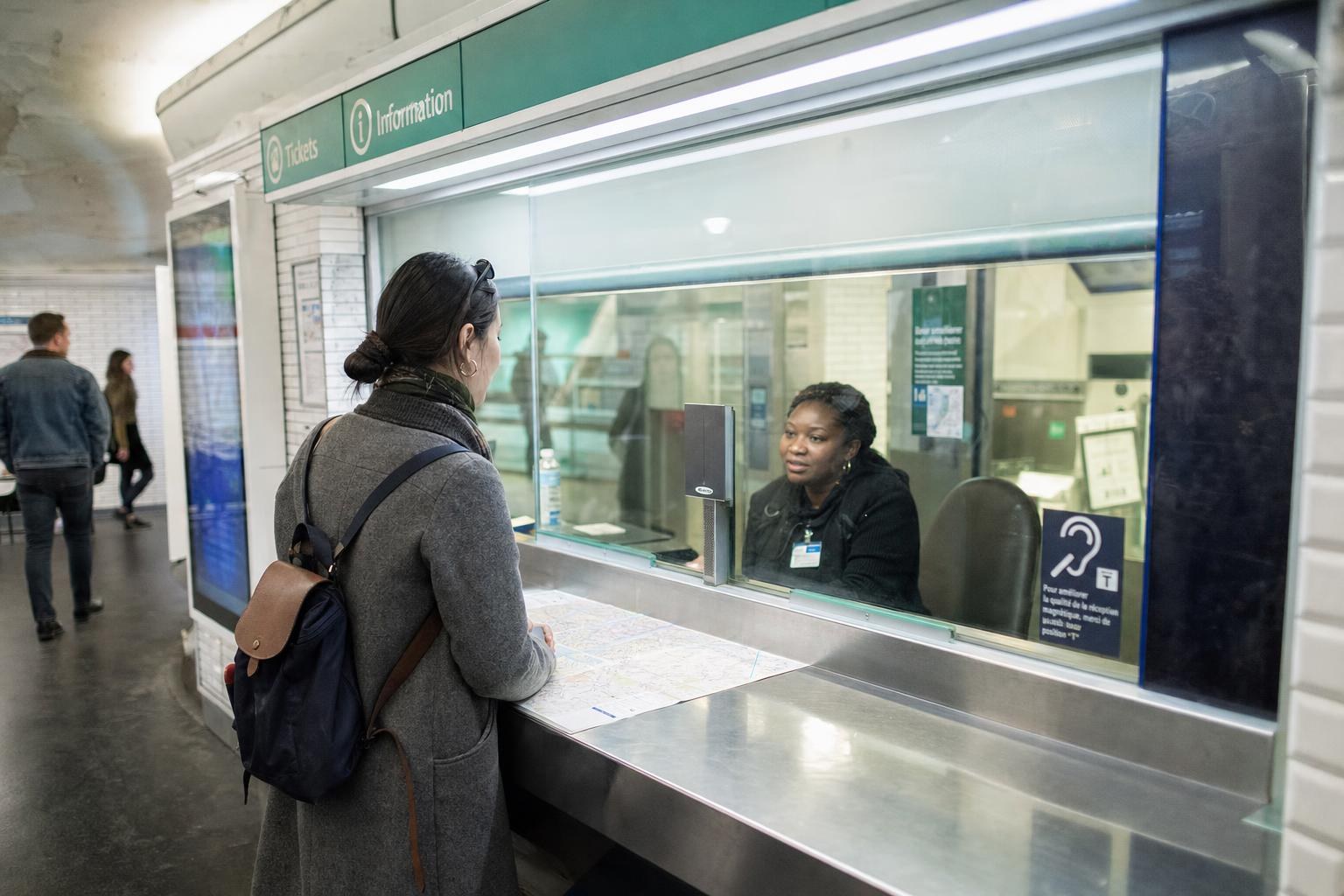 AI-generated illustration: A traveler asking for directions at a Paris metro station information desk